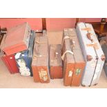 Seven vintage suitcases, some with travel labels and shipping labels.