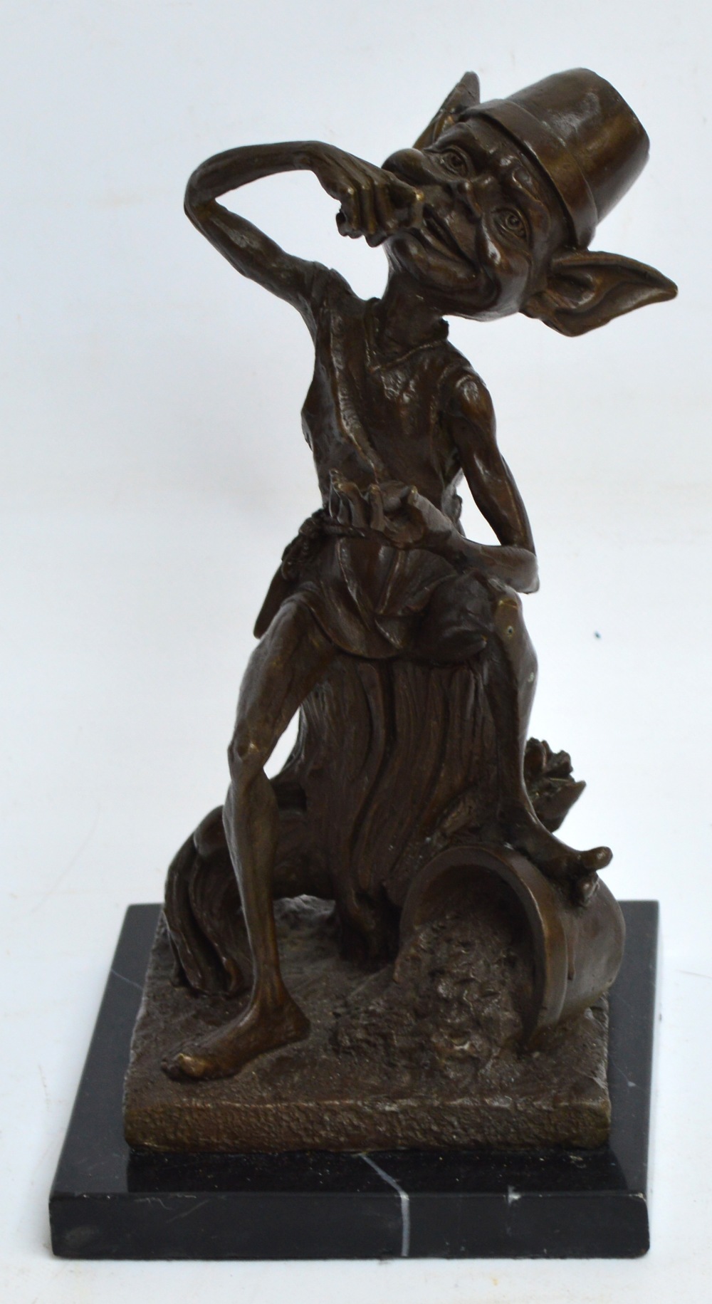 A bronze figure of a goblin seated on a tree stump eating berries and playing with a ladybird,