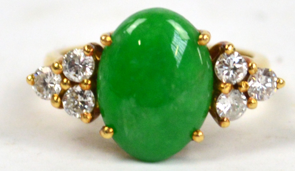 An 18ct yellow gold ring set with oval green jadeite stone flanked by six brilliant cut diamonds,