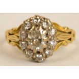 A yellow metal diamond cluster ring, the central stone approx 0.6cts, with foliate decorated arms,