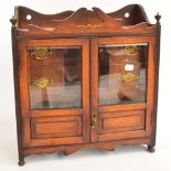 An Edwardian oak smoker's cabinet with glazed doors enclosing drawers,