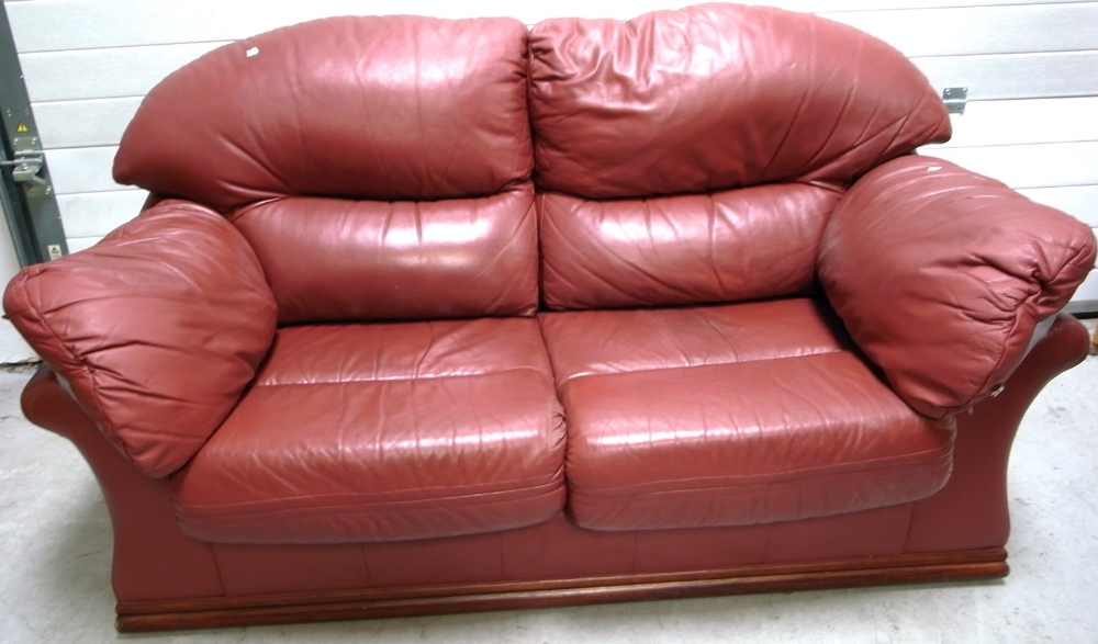 A contemporary maroon leather two seat sofa on wooden plinth base, approx width 170cm.