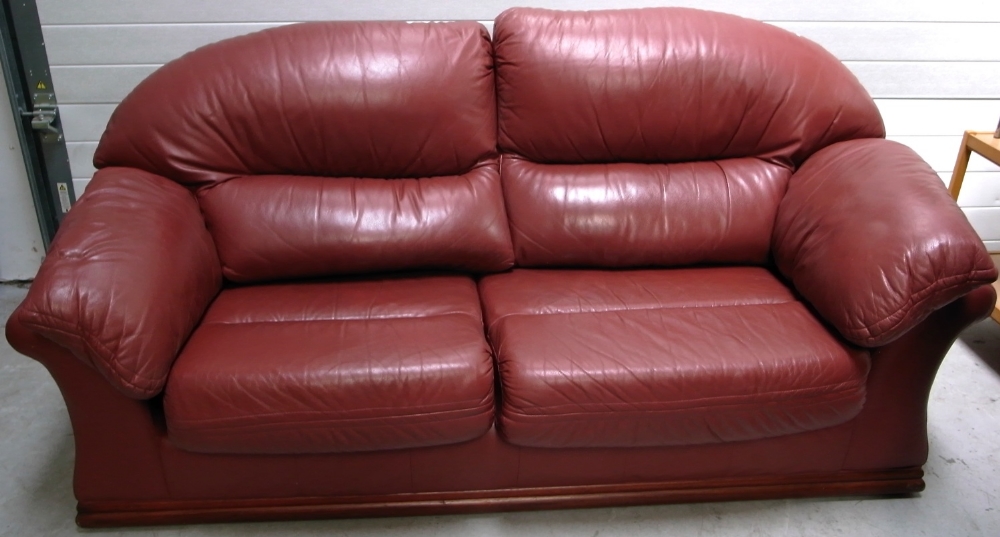 A contemporary maroon leather three seat sofa on wooden plinth base, approx width 200cm.