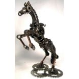 A modern sculpture of a rearing horse mounted on a base of three cogs and manufactured from various