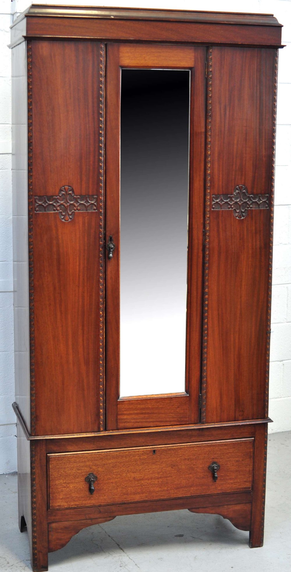 A mahogany single door wardrobe, glazed central door above lower drawer and bracket feet,