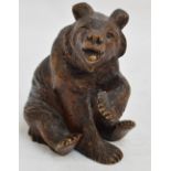 A late 19th century Black Forest carved figure of a seated bear with one paw raised, with glass