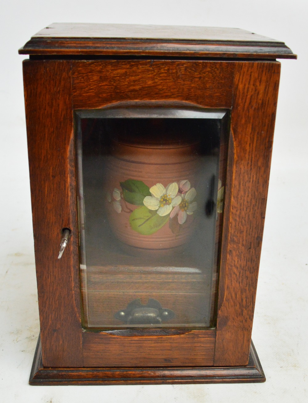An Edwardian oak smoker's cupboard with bevelled glass door enclosing a tobacco jar and drawer,