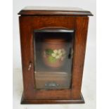 An Edwardian oak smoker's cupboard with bevelled glass door enclosing a tobacco jar and drawer,