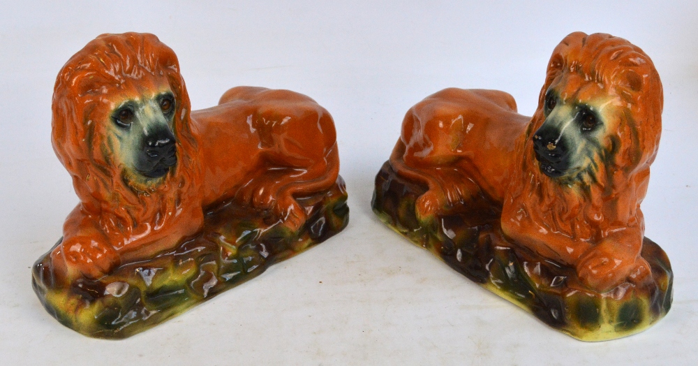 An opposing pair of late 19th century Staffordshire figures of recumbent lions on naturalistic