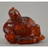 A Japanese carved amber netsuke modelled as a bearded gent reclining on two ceramic vessels,