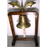 A brass ships bell on a wooden frame mounted with brass dolphins and brass letters to the top