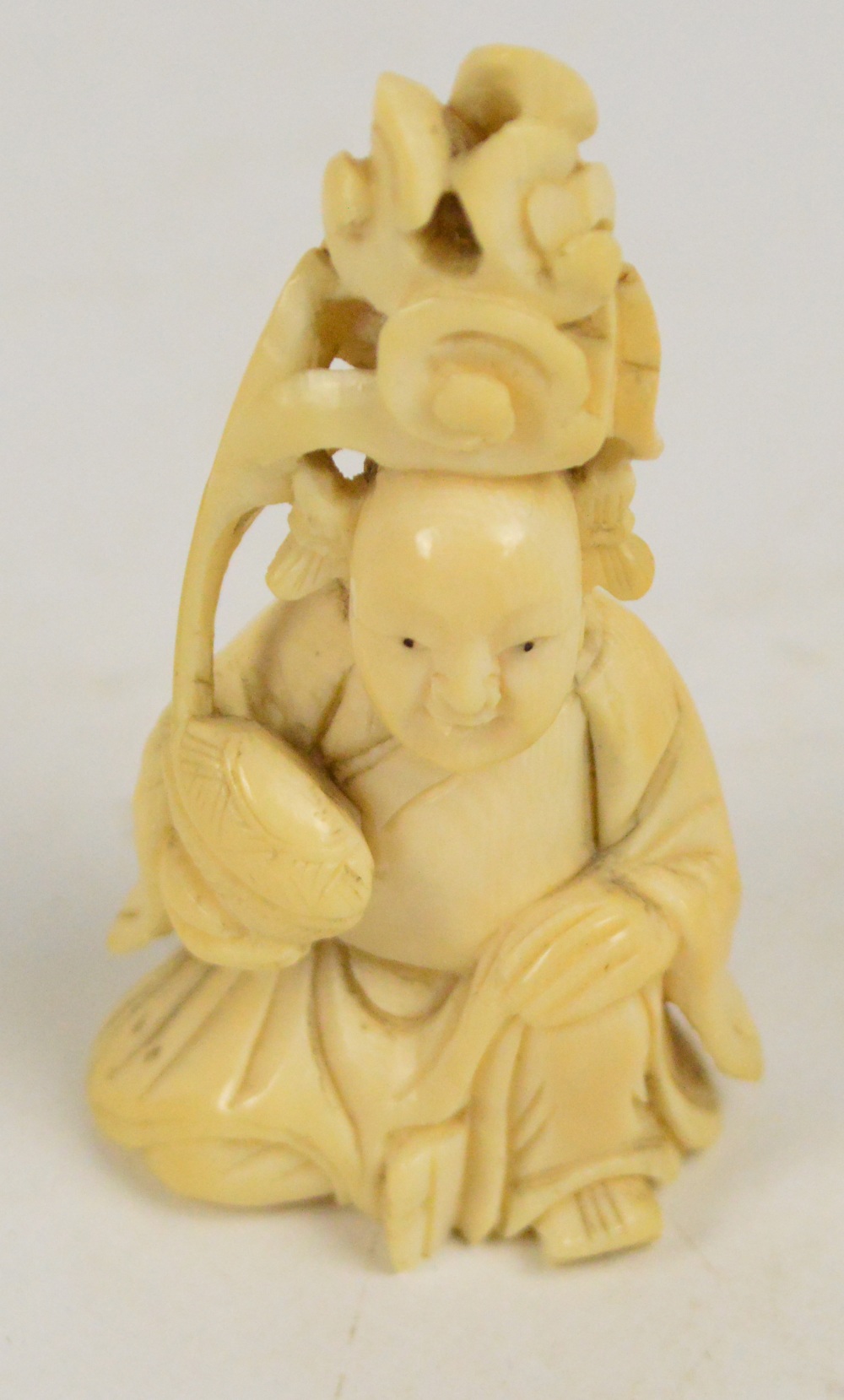 A 19th century Japanese carved ivory okimono depicting a seated man holding a blossoming nut,