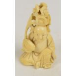A 19th century Japanese carved ivory okimono depicting a seated man holding a blossoming nut,