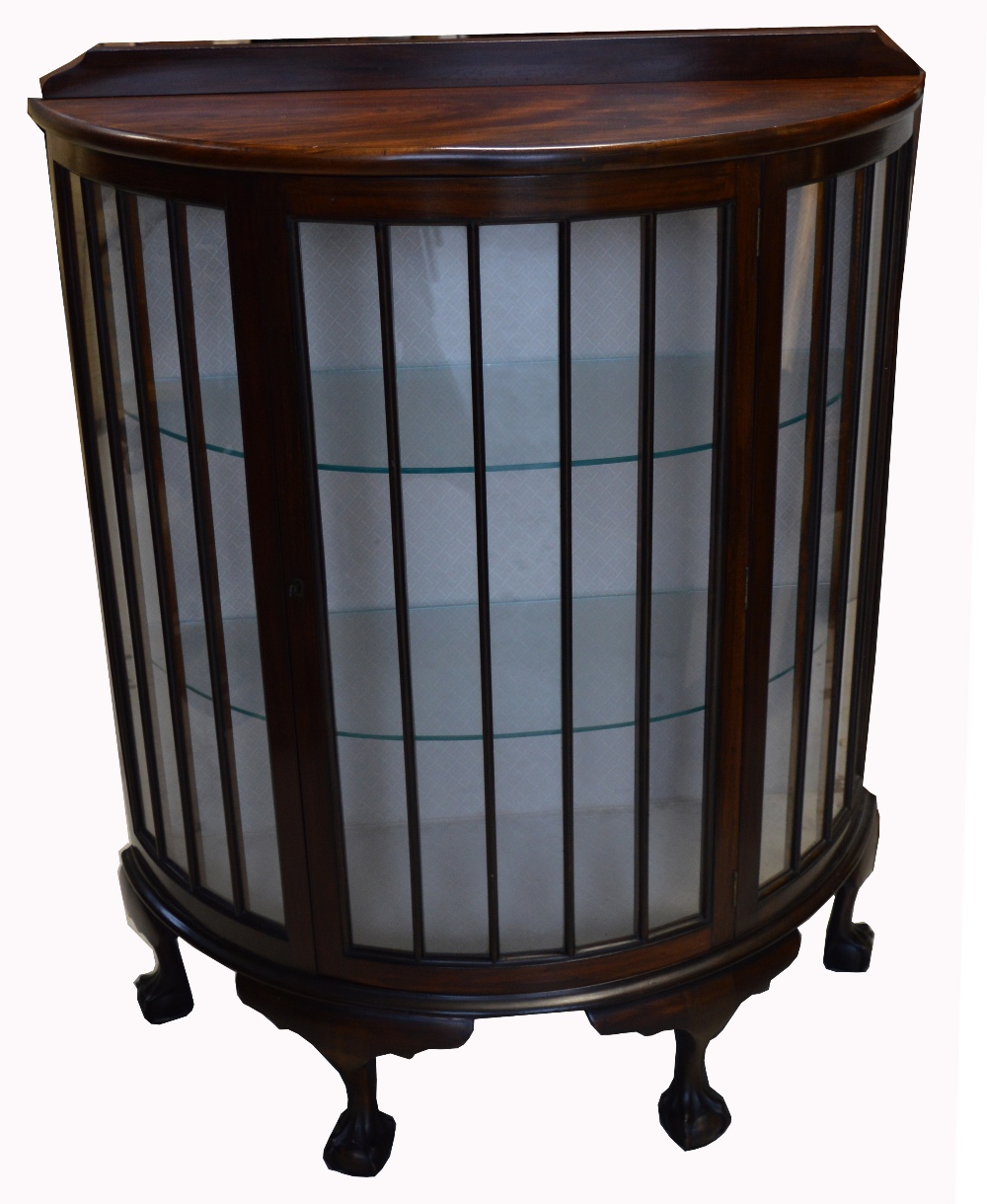 An early 20th century bow front display cabinet raised on ball and claw feet,