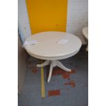 A circular extending cream painted dining table raised on turned central column with four outswept