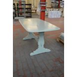 A pale green painted refectory type table raised on shaped end supports united by a central