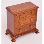 A contemporary miniature chest of three graduated drawers with inlaid detail and ogee bracket feet,