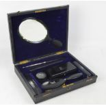 A leather cased ebony travelling set comprising rectangular trinket box, hand mirror, hairbrush,