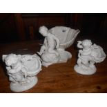Three Porcelain Figures of Cherubs Holding Aloft Shells.