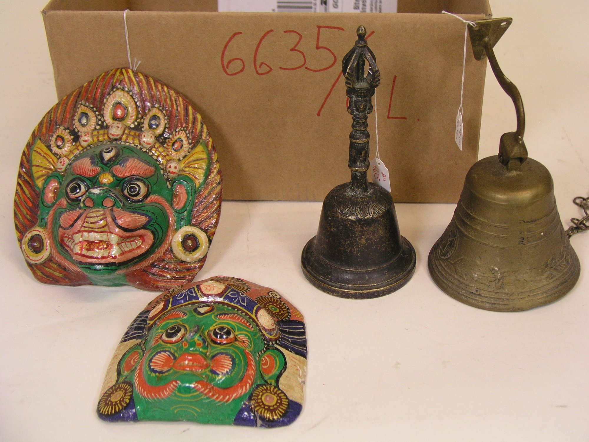 Drei nepalesische Masken. Pappe, bemalt, je ca. 18 x 16cm; beschädigt. Dazu: zwei Glocken,19,5 und