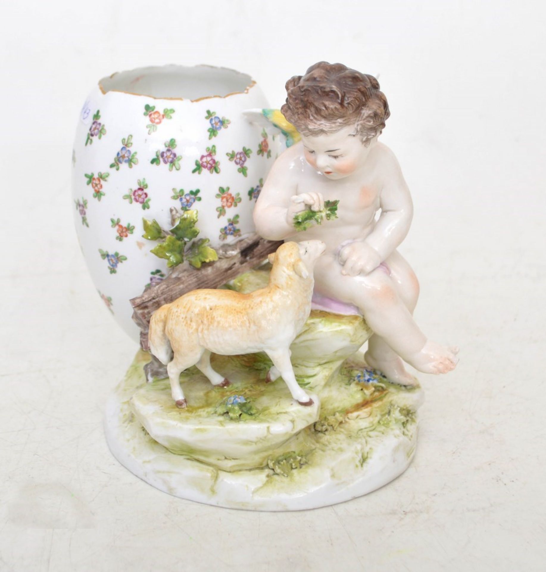 Putto mit Lamm  ovaler Sockel, Putto auf Steinsockel sitzend, dahinter buntes Ei als Vase, mit