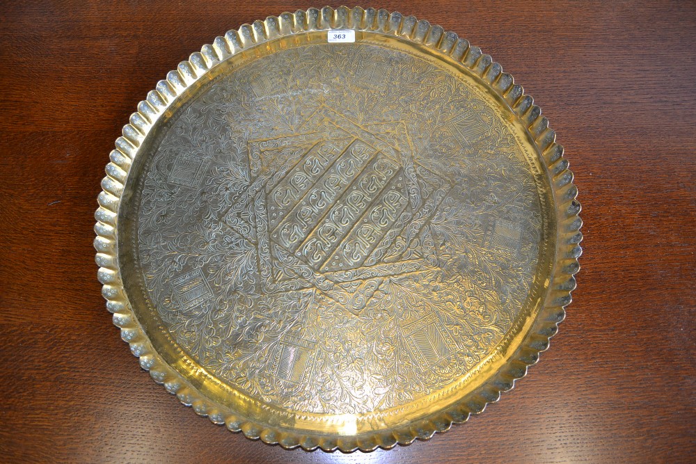 An Arabic brass charger, chased with script, foliage and precious objects, 57cm diameter