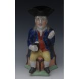A Staffordshire Squire jug, seated on a corner chair, wearing a black tricorn hat,