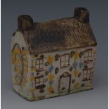 An early 19th century Pratt money box, in the form of a cottage, decorated in ochre, tan and blue,