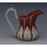 A Victorian cranberry glass jug, overlaid in white with stiff leaves, picked out in gilt,