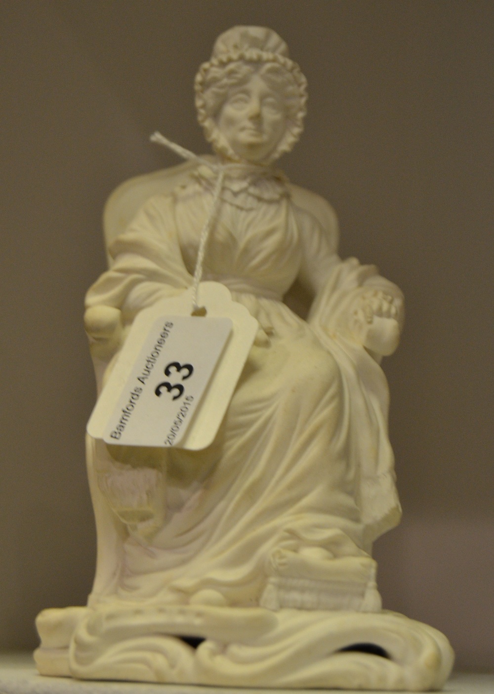 A Derby biscuit figure, of an elderly lady seated on a chair, one foot on a stool, scroll base,