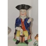 A Staffordshire Squire jug, seated on a corner chair, wearing a black tricorn hat,