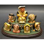 A Royal Doulton Henry VIII and his six wives miniature character jugs on a wood plinth ,