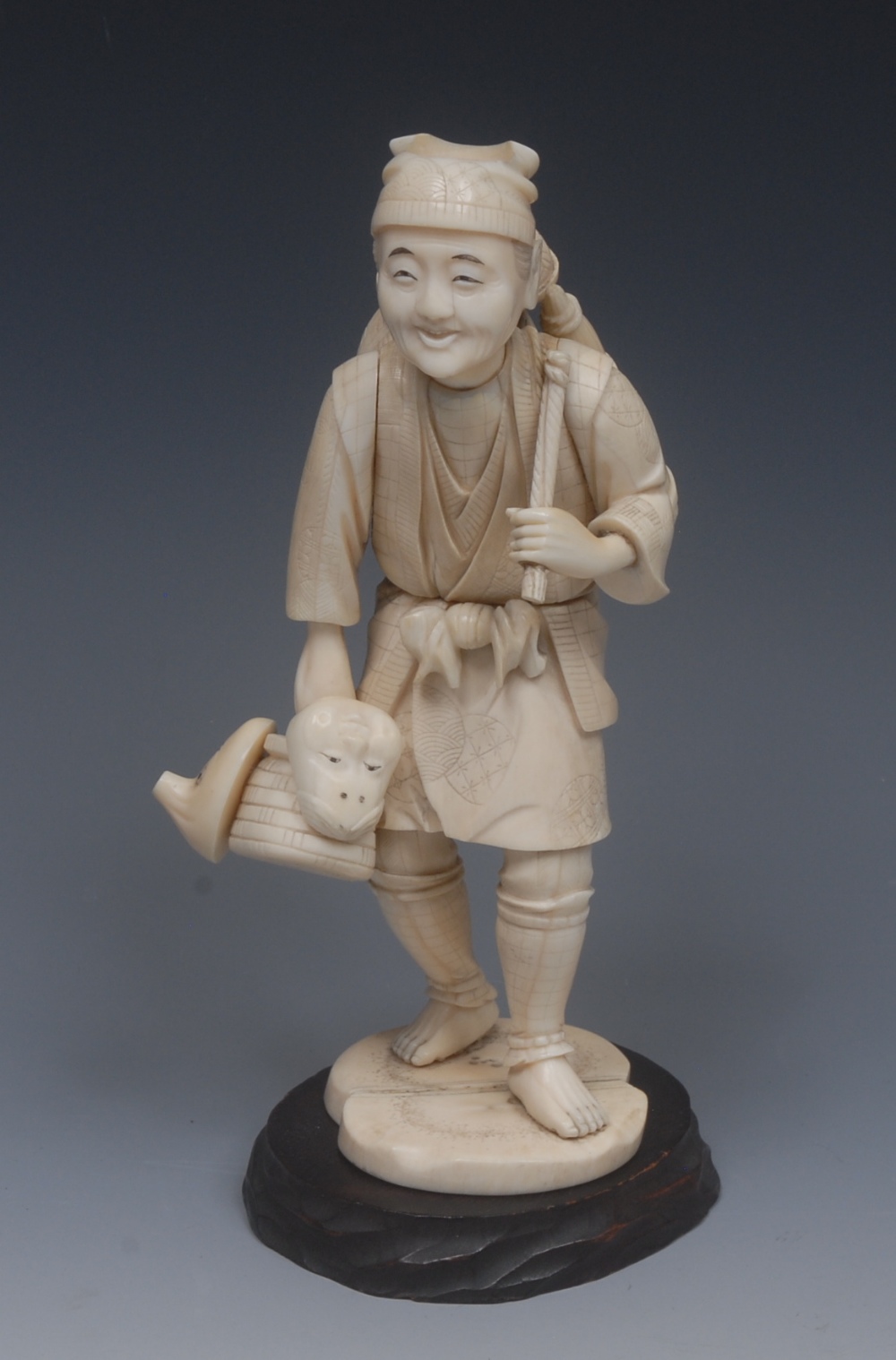A Japanese ivory okimono, of a street trader, standing with a basket over his shoulder,