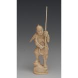 A Japanese ivory okimono, carved as a warrior, he stands, holding a staff, a shield on his arm,