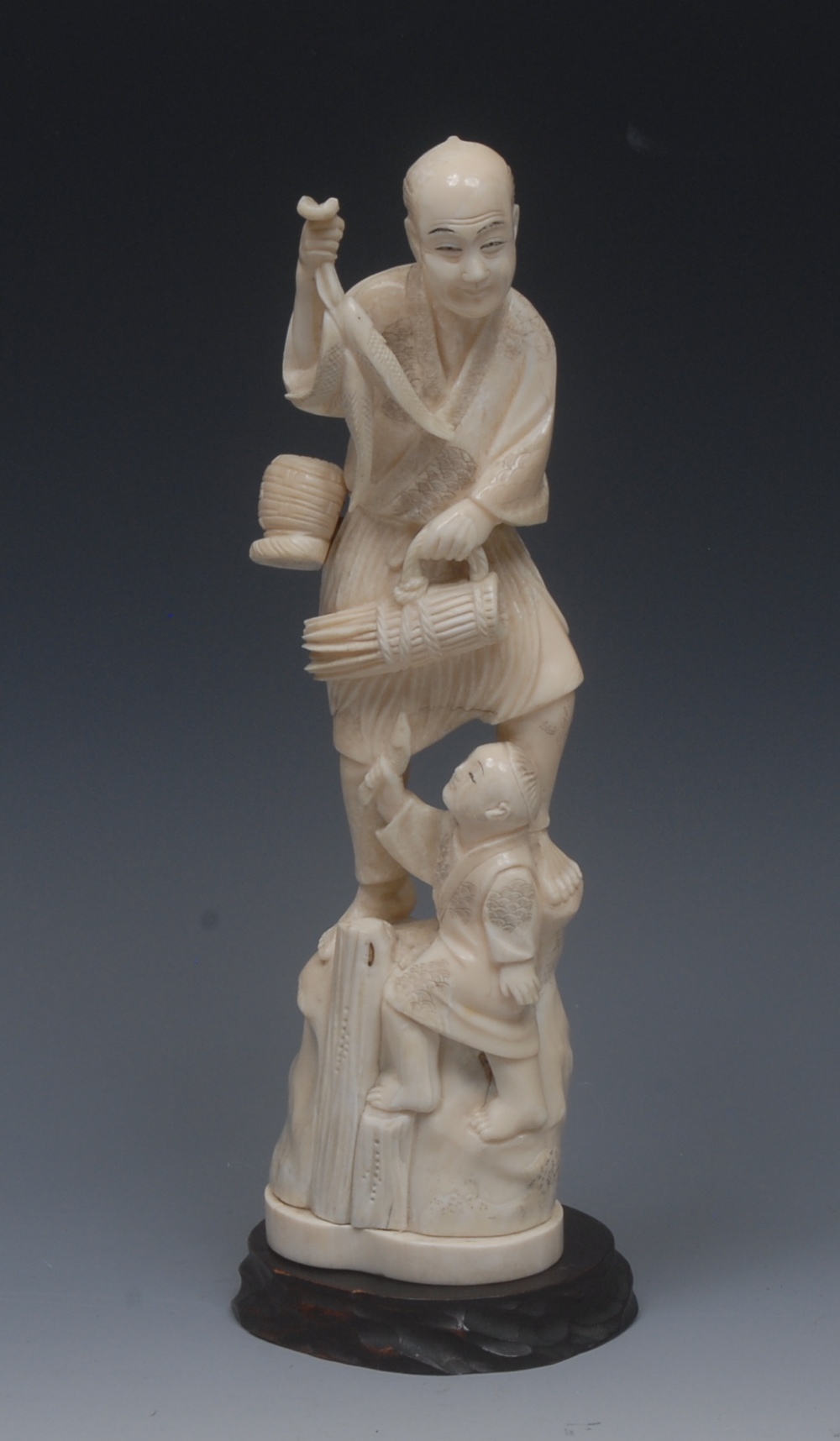 A Japanese ivory okimono, of a fisherman and his boy, he stands holding fish, the child at his feet,
