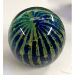 A Mdina domed glass paperweight, in mottled tones of green and yellow pulled through midnight blue,