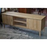 An Ercol style light oak media unit, oversailing top, central shelves flanked by cupboards,