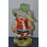 A Royal Crown Derby Mansion House dwarf, standing, wearing a broad brimmed hat, orange fancy shirt,