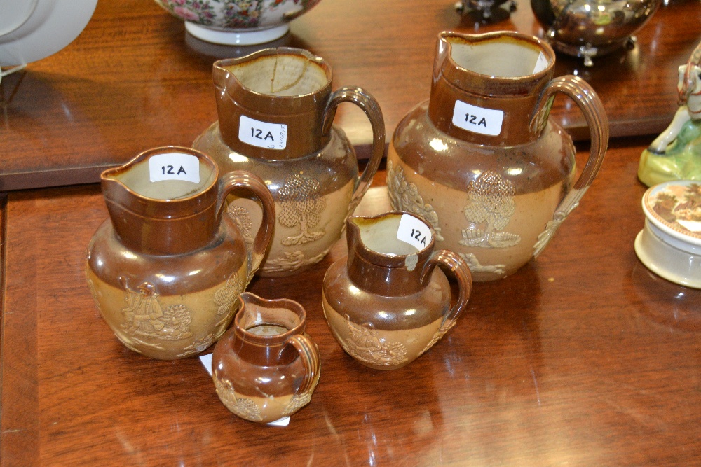 A graduated set of five Doulton Lambeth stoneware jugs, applied with jolly topers and trees,