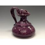A Bretby compressed ewer, glazed throughout in mottled tones of purple and puce, scroll handle,