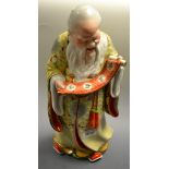 A Chinese porcelain figure, of a scholar, he stands, reading a scroll held in his hands,