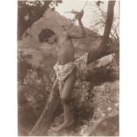 Gloeden, Wilhelm von: Boy with loin cloth on tree trunk Boy with loin cloth on tree trunk. Circa