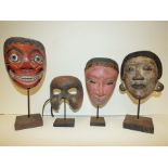 Four various painted Balinese masks with display stands