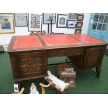 A reproduction oak desk having tooled crimson leathered top, on a base fitted drawers and acanthus