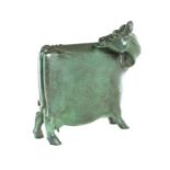 A bronze figure of a cow standing four square, it's head turned licking its back, green