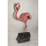 A late 20th century painted ceramic figure of a flamingo, with wire legs, mounted on a stone base,