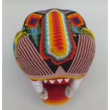 A Mexican Huichol Jaguar head mask, carved wood, bead covered in bright designs, 20cm high