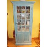 A modern sea blue painted softwood kitchen cabinet, the glazed door opening to reveal five fixed