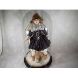 A dressed doll seated on a miniature chair within a period glass dome on ebonised circular base,