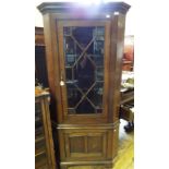 An oak floor standing corner cupboard, having a glazed door above a panel door,